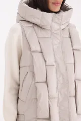 Chaleco acolchado color beige con diseño de cuadros, capucha amplia y cierre frontal oculto.