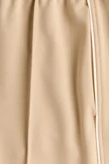 Pantalón de punto color beige con cintura elástica fruncida, piernas amplias, pliegues delanteros y ribetes laterales en color blanco.
