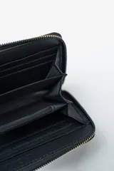 Billetera negra con cierre perimetral y tachas doradas decorativas en el borde frontal.