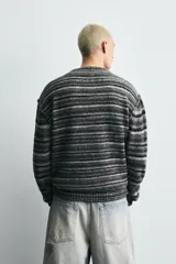 Cárdigan de punto con diseño de rayas horizontales en tonos grises y negros. Presenta un corte relajado, cuello en pico, cierre frontal con botones y acabados en rib en puños y bajo.