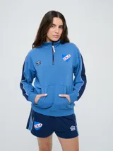 Buzo de felpa azul marino con medio cierre, cuello alto, bandas laterales en tono rosado y bolsillo frontal tipo canguro. Presenta el logo de Umbro y el escudo del Club Nacional de Football bordados.