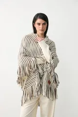 Poncho triangular tejido con diseño de rayas verticales en tonos crudo, marrón y negro, con detalle de hilo de lurex brillante y terminación de flecos largos en todo el borde.