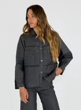 Chaqueta color gris oscuro con cierre frontal abotonado, cuello clásico, dos bolsillos de parche en el pecho y mangas largas con puños abotonados. Presenta detalles de costuras a la vista en contraste.