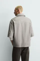 Sobrecamisa de corte relajado confeccionada en tejido efecto piel, con cuello solapa, manga corta, bolsillo plastrón en el pecho y cierre frontal con cremallera.