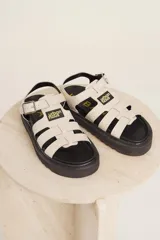 Sandalias de tiras anchas color crema con ajuste de hebilla al tobillo y suela track negra.