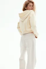 Campera con capucha y cierre frontal, color amarillo pálido, de corte cropped y holgado, con puños y bajo en punto acanalado.