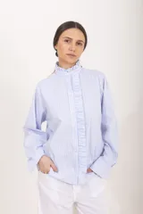 Camisa de manga larga a rayas celestes y blancas, con cuello alto mao y volados frontales a lo largo de la botonadura.