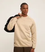 Suéter deportivo de hombre, color beige claro, con cuello redondo y manga larga raglán. Presenta una textura acolchada con un patrón ondulado en relieve.