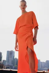 Vestido midi color naranja de la colección ZW de Zara, con cuello redondo, manga corta y detalle de tejido drapeado con volados en el delantero. Cuenta con cierre en la espalda con abertura y botón.