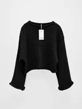 Sweater de punto acanalado color negro, con diseño oversize, cuello bote y mangas amplias tipo murciélago. Presenta un corte crop y terminaciones enrolladas en los puños y el ruedo.