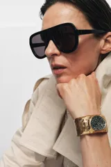 Pulsera rígida de metal con acabado texturizado y labrado en tono dorado, con una aplicación central circular incrustada de cristales negros brillantes.