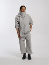 Buzo hoodie oversize de felpa de algodón color gris, con capucha y bufanda integrada que envuelve el cuello. Presenta cierre frontal y bolsillos canguro.