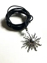 Collar con dije de sol en acero quirúrgico y lazo largo de cuero negro ajustable.