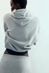 Sudadera gris con capucha y manga larga. Presenta un bolsillo canguro en la parte delantera y un estampado en azul marino con el texto "LOS ANGELES CALIFORNIA EST. 1975". Los acabados son de rib.