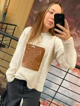 Sweater tejido de punto en color crema, con corte holgado y manga larga. Presenta un aplique rectangular central de cuero genuino con un mapa grabado.
