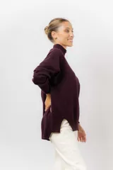 Sweater de tejido de punto color beige, con cuello alto, hombros caídos, mangas largas con puños acanalados y tajos laterales en el ruedo.