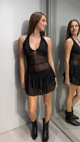 Vestido corto negro con escote halter y diseño de paneles transparentes en el torso. La falda presenta un diseño de doble volado en tejido semitransparente.