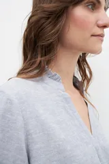 Blusa celeste de lino con cuello mao con volados, mangas cortas y cierre frontal con botones.