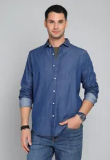 Camisa de jean azul con botones blancos, mangas largas con puños doblados y corte clásico.