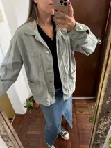 Campera de jean verde claro de corte oversize, con bolsillos frontales con solapa en el pecho y bolsillos aplicados en la parte inferior. Cierre frontal con botones metálicos y cuello camisero.