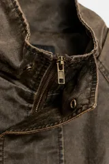 Chaqueta encerada color marrón con efecto lavado, cuello subido y manga larga. Cuenta con bolsillos frontales de plastrón y cierre de cremallera oculto por solapa con botones a presión. Los puños reversibles dejan ver un forro interior con estampado a cuadros.