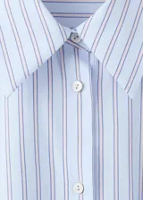 Camisa de popelina celeste a rayas, de corte oversize, con cuello camisero, mangas largas y aplicaciones de pedrería y lentejuelas brillantes distribuidas por toda la prenda.