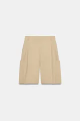 Bermuda larga cargo de color beige, confeccionada en mezcla de algodón. Cuenta con tiro medio, cintura con trabillas, pinzas en el delantero y bolsillos estilo cargo en las piernas.
