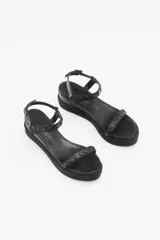 Sandalia negra con plataforma forrada en yute trenzado, de doble tira. La tira de la capellada está confeccionada en cuero con tachas texturadas y lisas de acabado níquel, mientras que el tobillo se sujeta con una segunda tira de cuero con las mismas tachas y hebilla metálica con grabada de la marca. Cuenta con una suela de caucho para mayor confort.