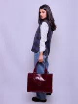 Cartera tipo tote de cuero vacuno con acabado brillante, diseño rectangular y doble asa de mano. Incluye un compartimento interno removible y detalle de logo grabado en el frente.