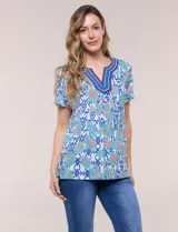 Blusa de manga corta con escote en V y pechera bordada. Presenta un estampado multicolor sobre base blanca, con pliegues frontales y aberturas laterales en el ruedo.