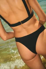 Conjunto de bikini negro de lycra texturada, compuesto por un corpiño triangular fijo con elástico interno bajo el busto y una bombacha vedetina con elástico interno.