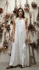 Vestido largo blanco de lino, con breteles finos y escote halter regulable. Presenta un aplique de flor de lino y cuero con strass en el centro, y tajo lateral con tul bordado.