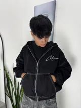 Campera de jean negra con cierre frontal, costuras blancas a la vista y logo bordado en el pecho. Posee capucha y puños elásticos.