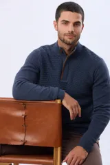 Buzo de punto color beige, con cuello alto y cierre frontal con cremallera y solapa de gamuza con botón. Presenta un tejido texturizado en el cuerpo y mangas lisas.