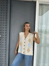 Chaleco tejido de punto con escote en V y cierre frontal de botones. Presenta un diseño de rombos en tonos beige y celeste sobre una base color crema.
