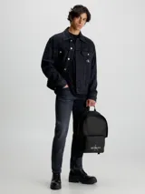 Mochila negra Calvin Klein Jeans con bolsillo frontal y logo estampado en blanco.