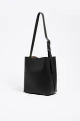 Bolso de hombro Bimba y Lola modelo Carlino, de estructura rígida y tamaño mediano, confeccionado en piel vacuna color tostado. Presenta asa regulable de piel con hebilla metálica y logo impreso en la parte inferior.