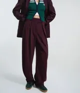Pantalón de sastrería corte barrel, color marrón oscuro, con pliegues delanteros, cintura con cierre desplazado y piernas anchas.