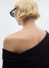 Vestido corto negro de diseño asimétrico con escote de un solo hombro y manga larga. Presenta un corte entallado con detalle de lazo ajustable en la cintura y cierre de cremallera lateral.