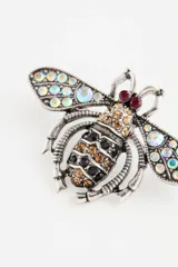 Pin en forma de abeja con acabado metálico envejecido, decorado con cristales brillantes en las alas y el cuerpo en tonos tornasol, ámbar y negro.