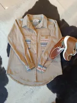 Camisa beige de manga larga, con bolsillos frontales en el pecho, puños y detalles interiores con diseño de guardas a rayas multicolor. Cuenta con cierre frontal de botones y cuello camisero.