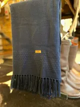 Ruana de punto color azul marino, con flecos en los extremos y una pequeña etiqueta de cuero sintético con el logo de la marca en el centro.