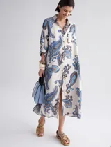 Vestido camisero largo con estampado paisley en tonos celeste, azul y marrón. Tiene cuello camisero, mangas largas con puños abotonados, cierre frontal con botones y un bolsillo en el pecho.