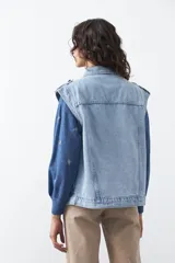 Chaleco de jean en tono celeste claro, con corte recto, cuello camisero, cierre frontal con botones metálicos y costuras visibles.