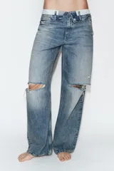 Jeans de tiro medio con diseño de cintura doblada, cinco bolsillos y cierre frontal con cremallera y botón metálico. Presenta un acabado desgastado con roturas en las rodillas y corte recto.