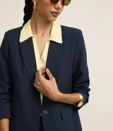 Blazer de sastrería color azul marino, con solapas clásicas, cierre frontal de un solo botón con detalle metalizado y bolsillos simulados. Confeccionado en una mezcla de viscosa y poliéster, presenta un corte recto y estructurado.
