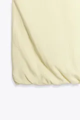 Top corto color crema confeccionado con lino, escote pico y tirantes finos. Detalle de espalda abierta con tira elástica horizontal y bajo abullonado con elástico interior.