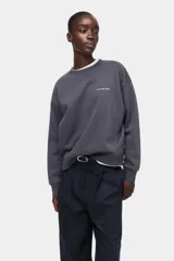 Buzo oversize gris oscuro con cuello redondo, hombros caídos y pequeño texto estampado en el pecho. Presenta puños y bajo con ribete acanalado.