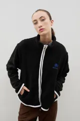 Campera de sherpa color beige con cuello alto, cierre frontal completo y bordado a contra tono en el pecho.