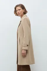 Tapado clásico de corte recto en color beige, con solapas, cierre frontal de botones y bolsillos laterales. Presenta un diseño minimalista y elegante.
